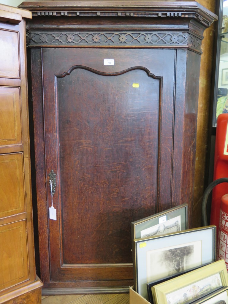 A George III oak corner cupboard, the dentil cornice over a blind fret carved frieze over a panelled