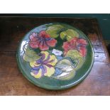 A Moorcroft Pottery charger in the Hibiscus pattern with red and yellow flowers, initialled