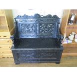A Victorian carved ebonised settle, with lunette and foliate design, hinged seat and panelled