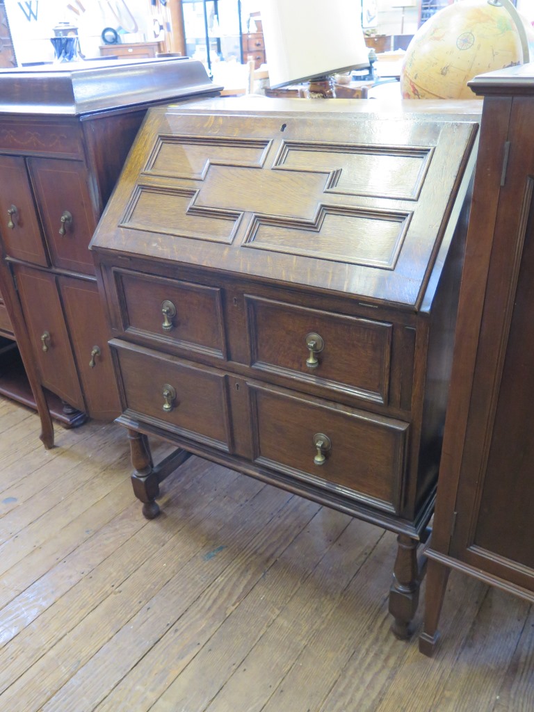 An 1930s oak bureau, the panelled slope enclosing pigeonholes over two graduated drawers on turned