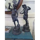 A pair of late 19th century bronzed metal figures of a girl sewing her petticoat and a boy holding a