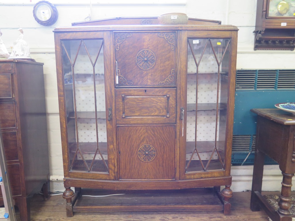 An oak secretaire display cabinet, 1940s, the central cupboard door above a secretaire drawer and