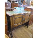 An oak side cabinet, with leather inset top over a pair of panelled doors on barley-twist legs