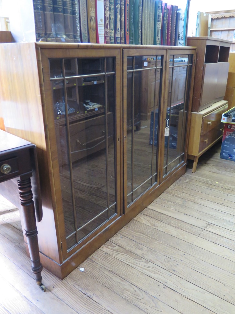 A walnut three door glazed display cabinet on a plinth base, by Heal's of London, label to one