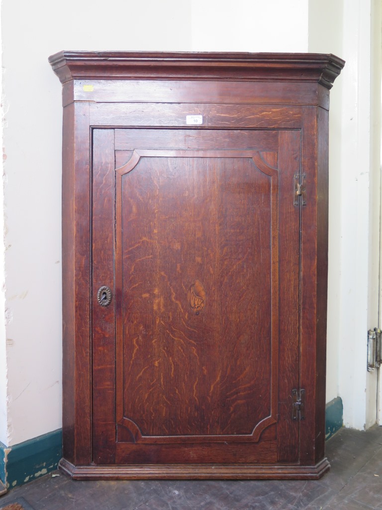 A 19th century corner cupboard, the cavetto cornice over a shell inlaid panelled door enclosing