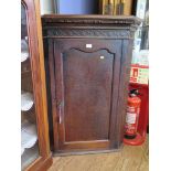 A George III oak corner cupboard, the dentil cornice over a blind fret carved frieze over a panelled