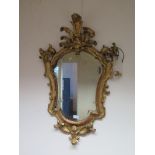 A Florentine style giltwood wall mirror, the shaped plate within a foliate spray carved frame 86cm x