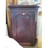 A George III oak corner cupboard, the dentil cornice over a blind fret carved frieze over a panelled