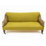 A LATE 19TH / EARLY 20TH CENTURY HOWARD STYLE SOFA with green upholstery and standing on turned fore