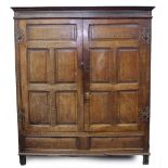 AN 18TH CENTURY STYLE OAK PANELLED CUPBOARD with shaped brass hinges, standing in stile feet,