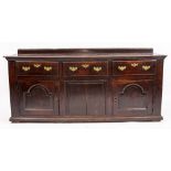 A GEORGIAN OAK DRESSER BASE with three frieze drawers above two cupboard doors and raised on a