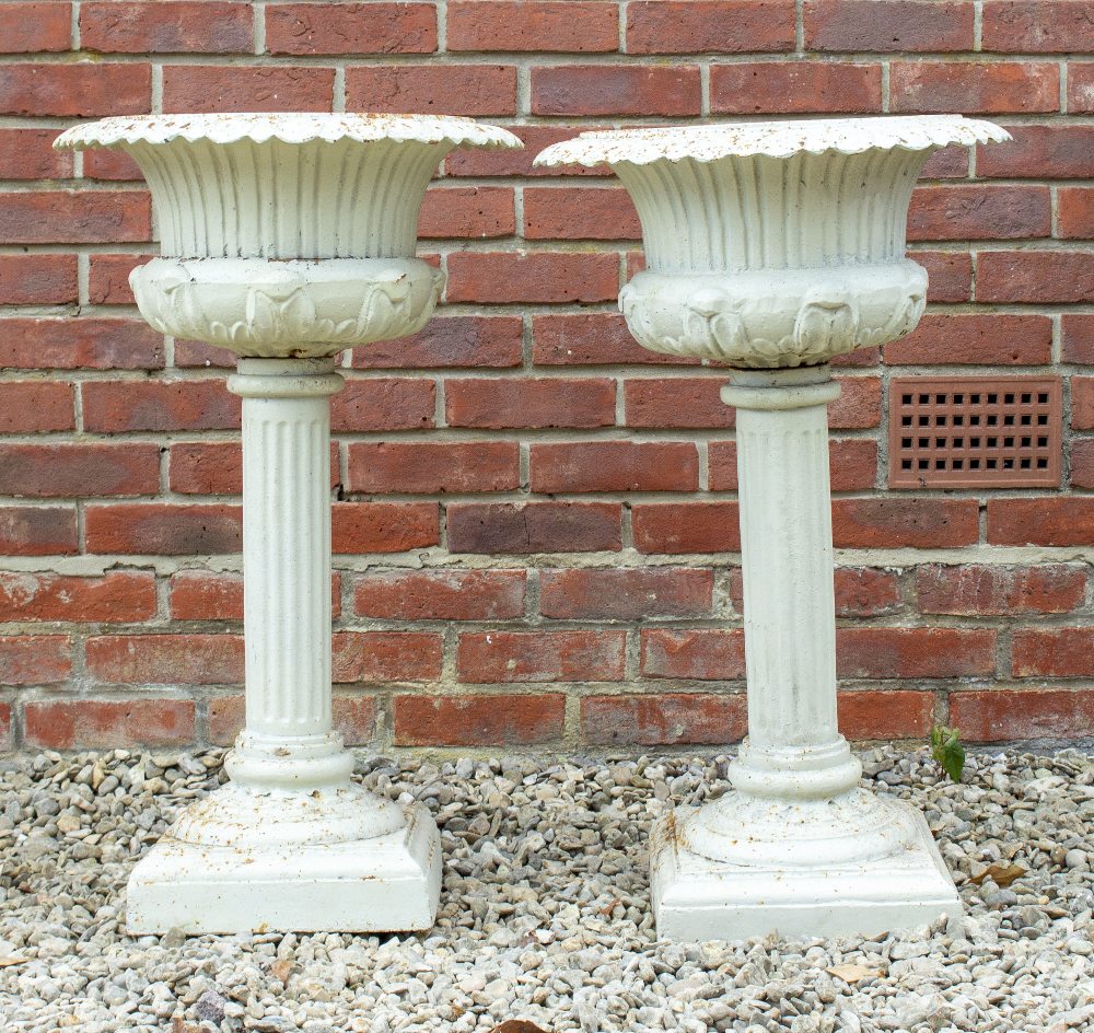 A PAIR OF CAST IRON GARDEN URNS with egg and dart decorated rims on fluted column supports and