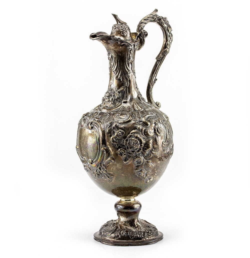 A VICTORIAN SILVER WATER JUG with repousse decoration and a scrolling handle on a circular base,