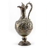 A VICTORIAN SILVER WATER JUG with repousse decoration and a scrolling handle on a circular base,