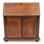 AN OAK BUREAU with a fall front above two panelled doors below, 101cm wide together with an oak