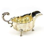 A SILVER SAUCE BOAT with ribbed body and acanthus topped scrolling handle, on three pad feet,