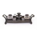 A BRONZED EMPIRE STYLE DESK STAND with central candlestick, inkwells and pen recesses with foliate