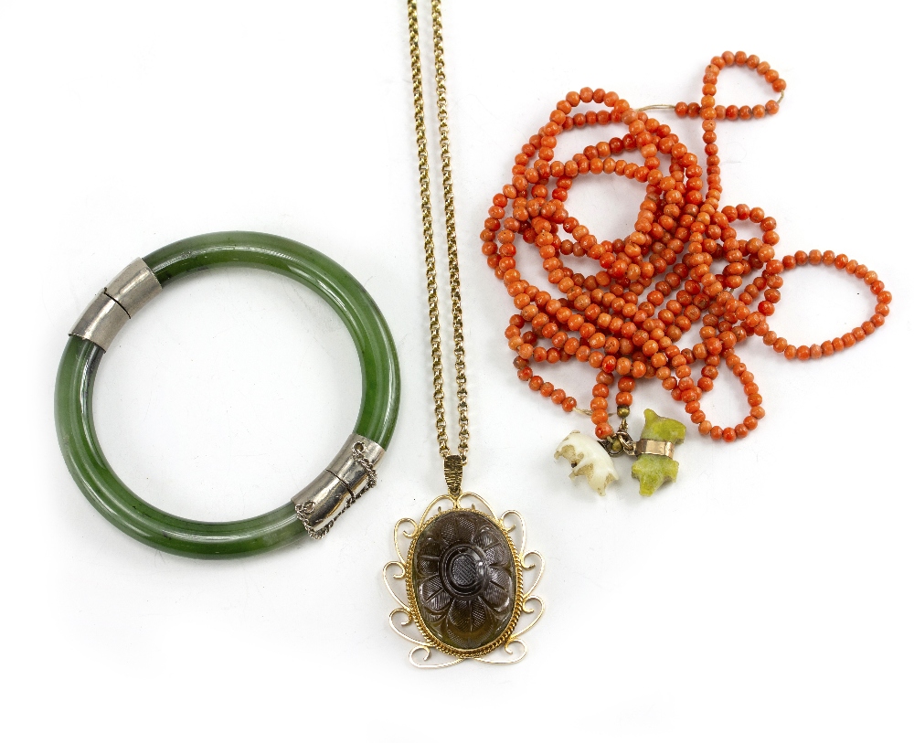 A STRING OF CORAL BEADS with carved pig charms, a Nephrite bangle with white metal mounts and a