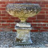 A RECONSTITUTED STONE SHALLOW CIRCULAR URN with floral cast decoration on a stand with one corner