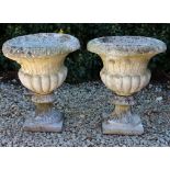 A PAIR OF RECONSTITUTED STONE GARDEN URNS with gadrooned bodies and on fluted circular bases, 41cm