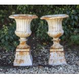 A PAIR OF SMALL CAST IRON FLUTED CAMPANA URNS on square section plinth bases, 29cm diameter x 51cm