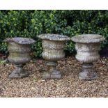 A SET OF THREE RECONSTITUTED STONE GARDEN URNS decorated with a floral band and on fluted bases (