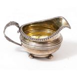A SILVER CREAM JUG with gadrooned rim and foliate decorated scrolling handle, standing on ball feet,