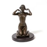 A BRONZE FIGURE OF A FEMALE NUDE the kneeling figure upon a cushion and putting on a necklace,