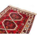 AN ORIENTAL RED GROUND RUG with five geometric medallions to the central field and within a banded