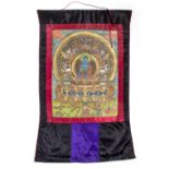 A TIBETAN THANGKA depicting a Buddhist deity on a silk background, 100cm x 60cm