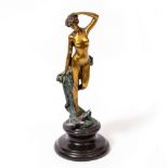 A GILT BRONZE FIGURE OF A FEMALE NUDE standing before a verdigris wave, on an ebonised plinth,