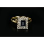A SAPPHIRE AND DIAMOND CLUSTER RING, the rectangular step-cut sapphire bordered by single-cut