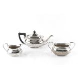 AN EDWARDIAN SILVER THREE PIECE TEA SERVICE, of half lobed design, the teapot with ebonised handle