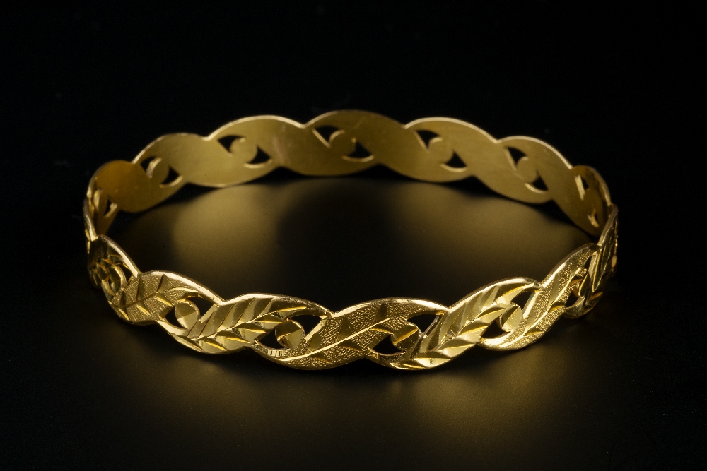 A YELLOW PRECIOUS METAL BANGLE, with pierced and foliate engraved decoration, inner diameter 6.3cm