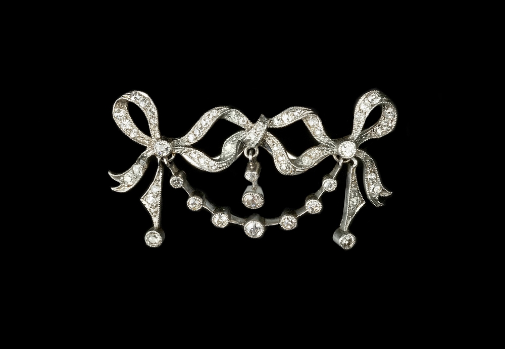 AN EARLY 20TH CENTURY DIAMOND SET BROOCH, designed as an openwork garland and loosely tied ribbon