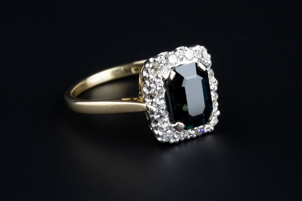 A SAPPHIRE AND DIAMOND CLUSTER RING, the rectangular step-cut sapphire bordered by single-cut