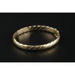 A THREE COLOUR PRECIOUS METAL BANGLE, of hinged oval twist design, stamped '750', inner diameter 6.