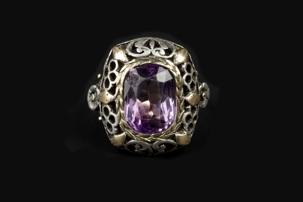 AN ARTS AND CRAFTS AMETHYST PANEL RING, the cushion-shaped panel pierced and engraved with foliage