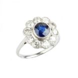 A SAPPHIRE AND DIAMOND CLUSTER RING, the circular mixed-cut sapphire in millegrain collet setting,