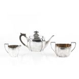 AN EDWARDIAN SILVER THREE PIECE TEA SET, of shaped oval form, with reeded borders, the teapot with
