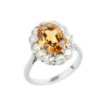 A TOPAZ AND DIAMOND CLUSTER RING, the oval mixed-cut topaz of brownish-orange hue, claw set within a