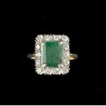 AN EMERALD AND DIAMOND CLUSTER RING, the rectangular step-cut emerald claw set within a border of