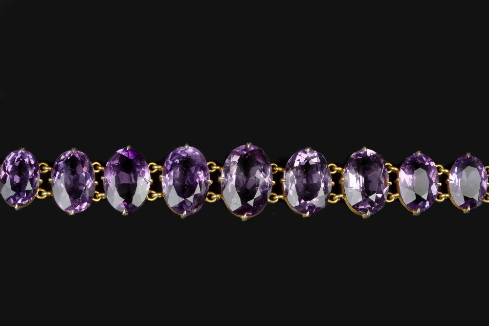 AN AMETHYST LINE BRACELET, the graduated oval mixed-cut amethysts in claw settings, gilt metal