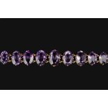 AN AMETHYST LINE BRACELET, the graduated oval mixed-cut amethysts in claw settings, gilt metal