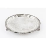 A LATE VICTORIAN SILVER SALVER, with shaped gadrooned border, on scallop and scroll cast feet, by