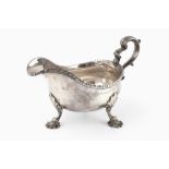A GEORGE III SILVER SAUCE BOAT with gadrooned border, scroll handle, and scallop cast feet, maker'