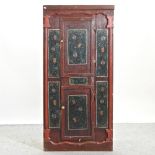An antique pine and red painted corner cupboard, with foliate decoration,