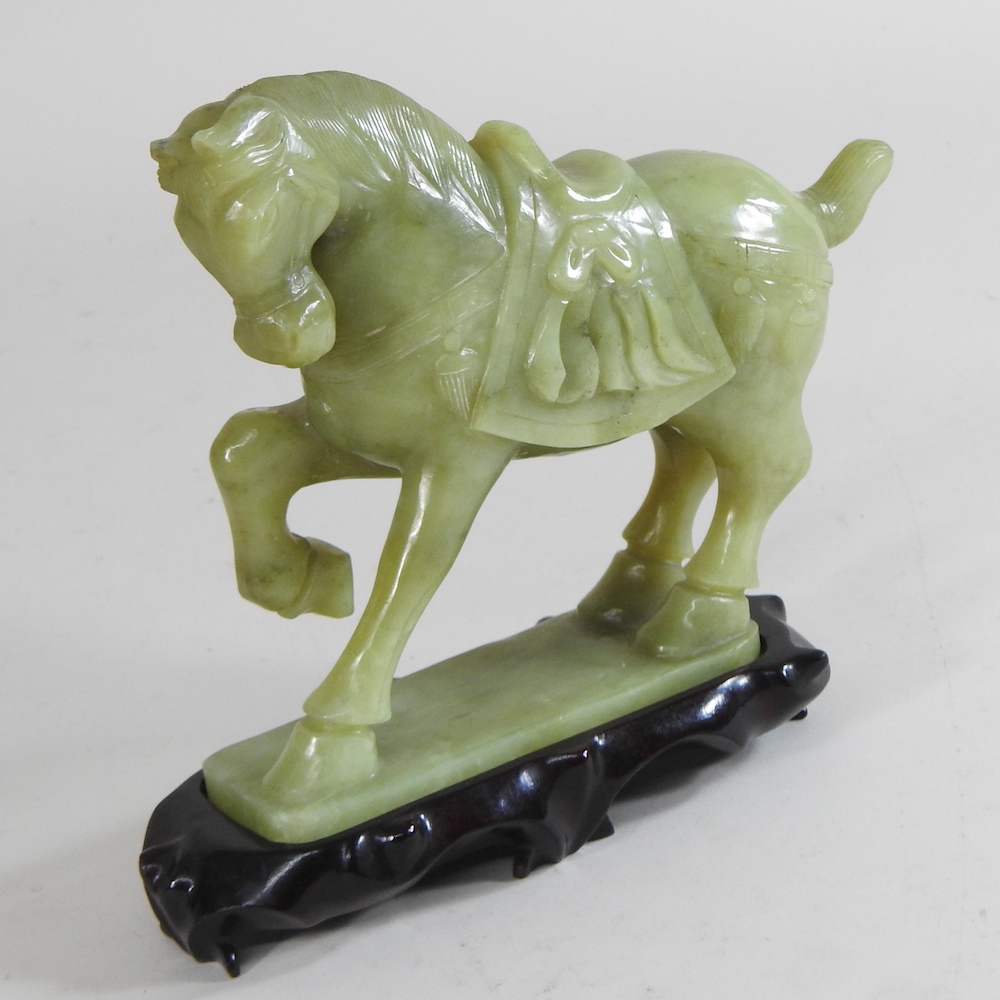A jade coloured hardstone horse, mounted on a wooden plinth,