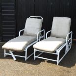 A pair of white painted metal garden sun loungers with loose cushions,