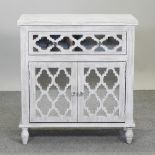 A modern white painted cabinet, with fret decoration and mirrored doors,